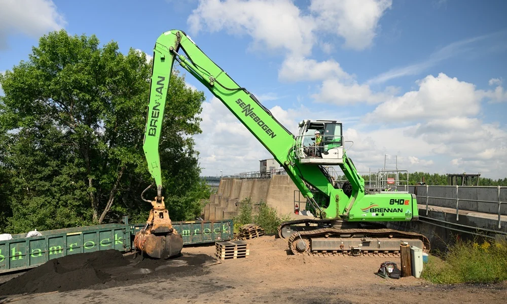A Brennan crew uses a green Sennebogen 840E material handler with a grapple to load a Shamrock container for remediation.