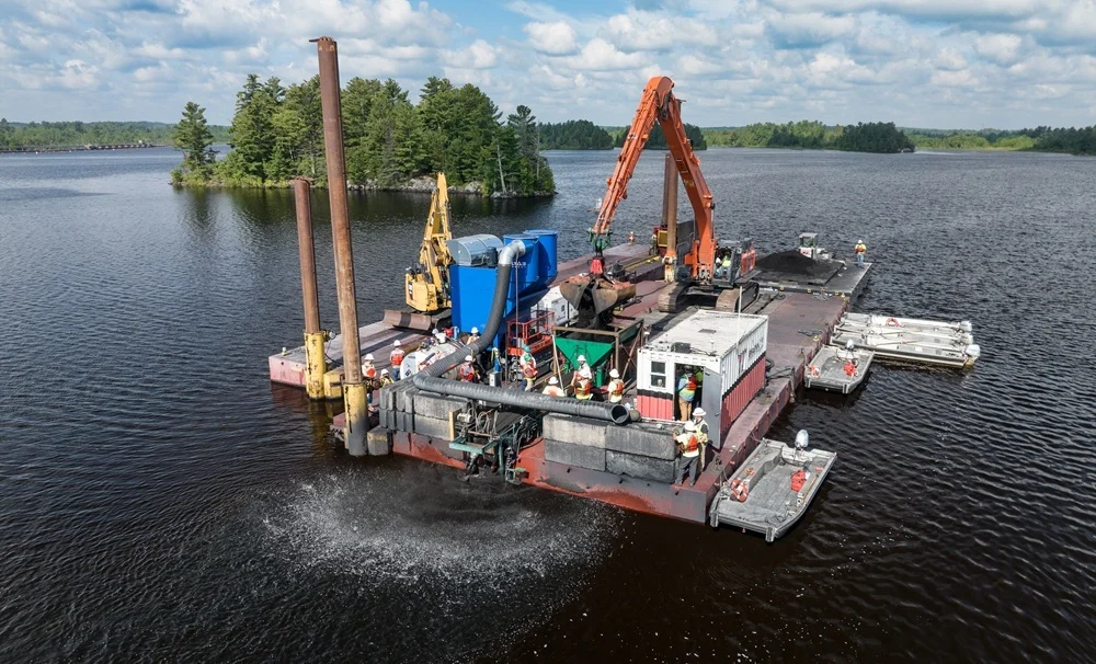 A Brennan crew operates construction equipment on a barge during an environmental remediation project on a lake.