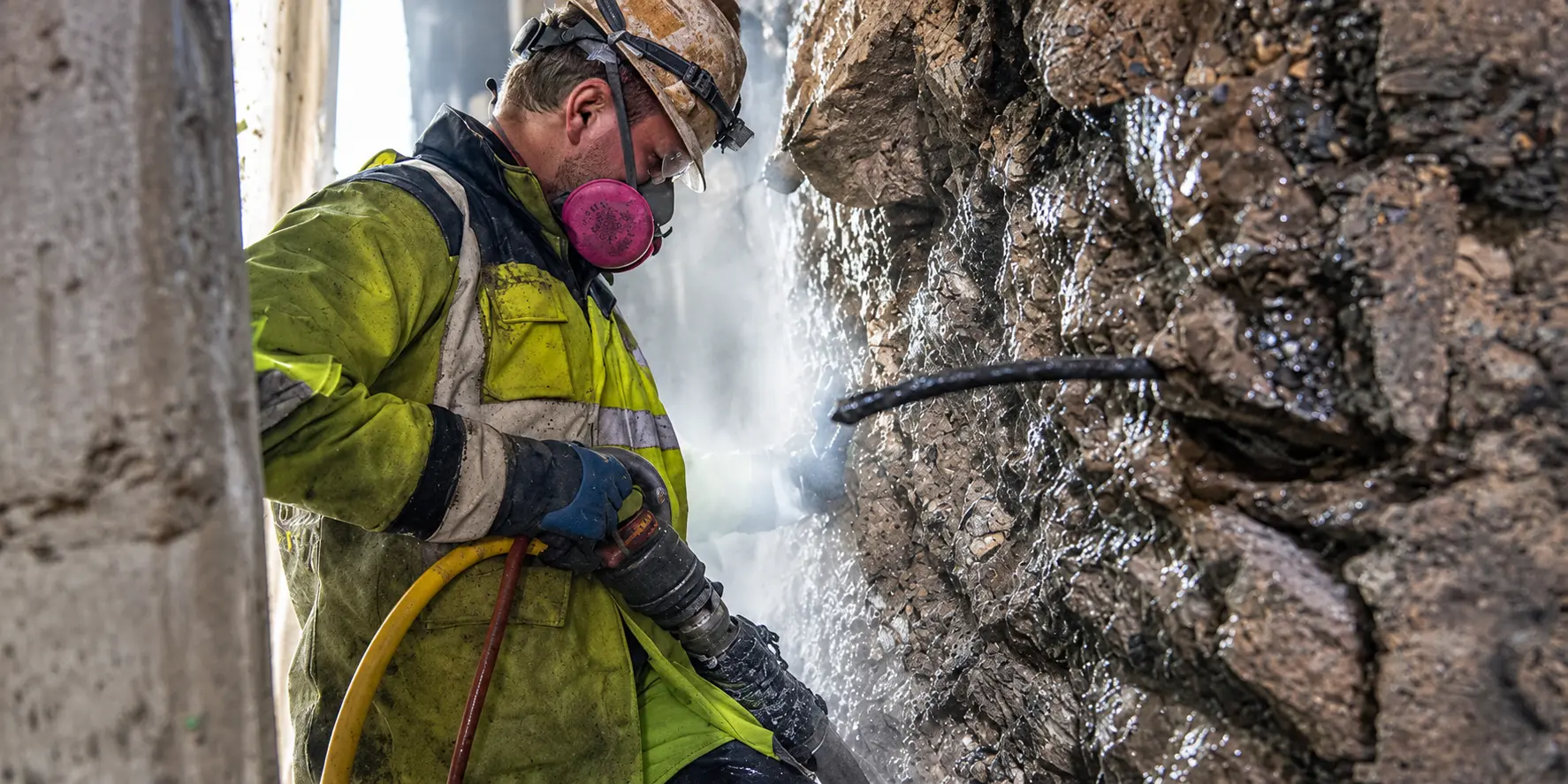 A Brennan worker uses a pneumatic hammer to chip away at a rock wall.