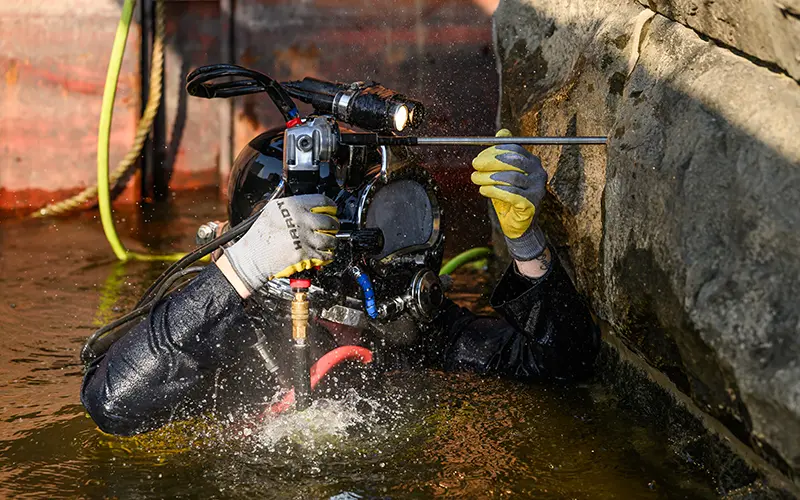 A Brennan crew member uses a pneumatic tool to repair an underwater stone wall.