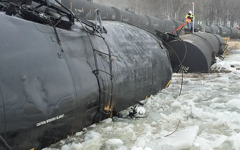 A Brennan worker observes derailed black tank cars resting in an icy river.